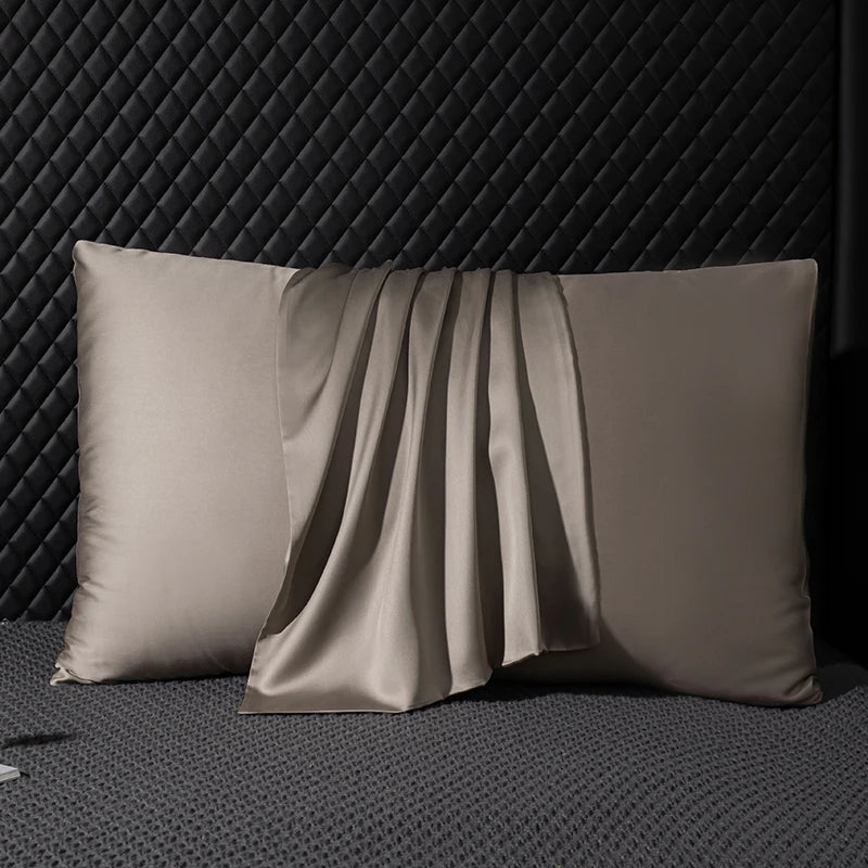 Two beige satin pillows on a textured dark surface with a geometric patterned wall in the background.