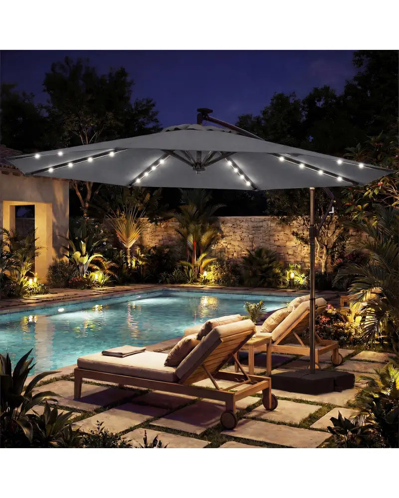 Outdoor patio with two lounge chairs under a large umbrella by a pool at night.