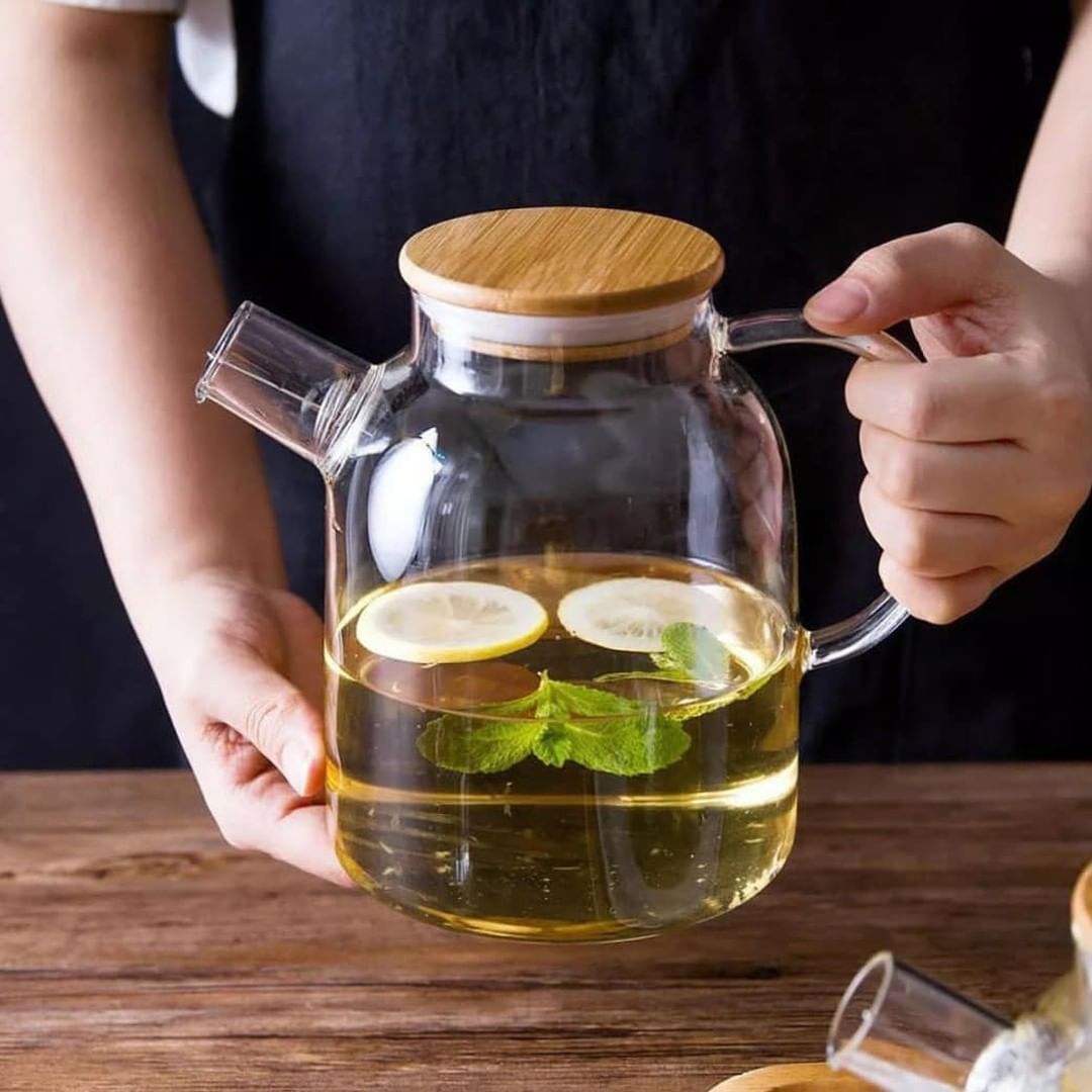 Glass teapot with wooden lid held by a person on a wooden surface