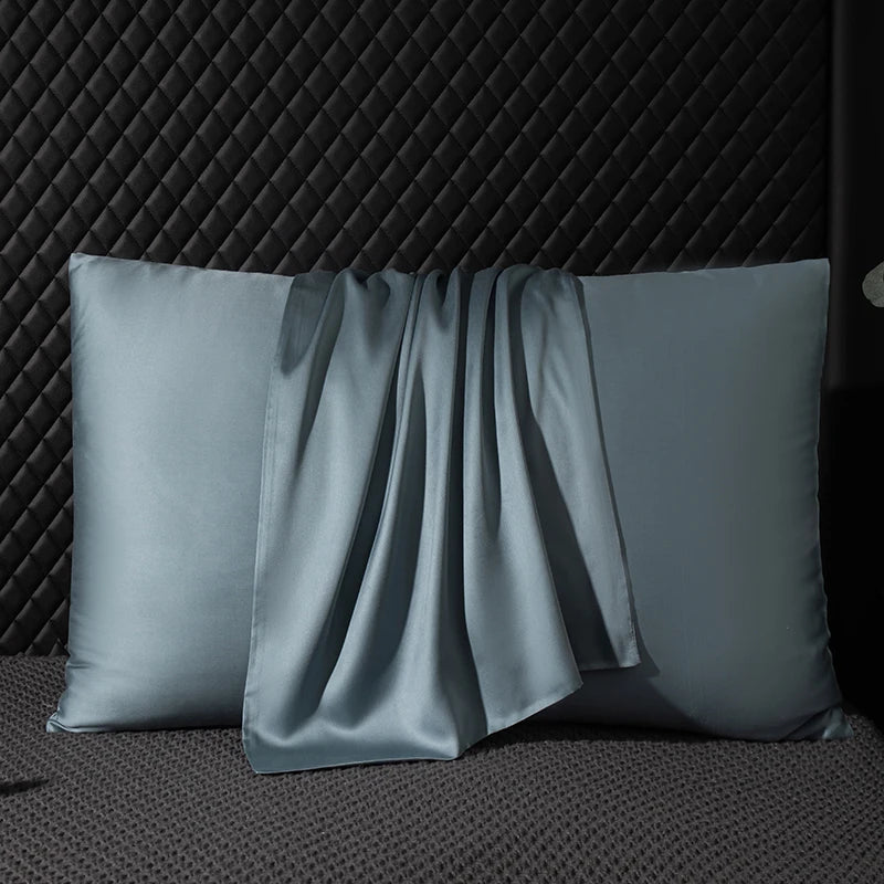 Two gray satin pillows on a textured dark surface with a black geometric patterned background.