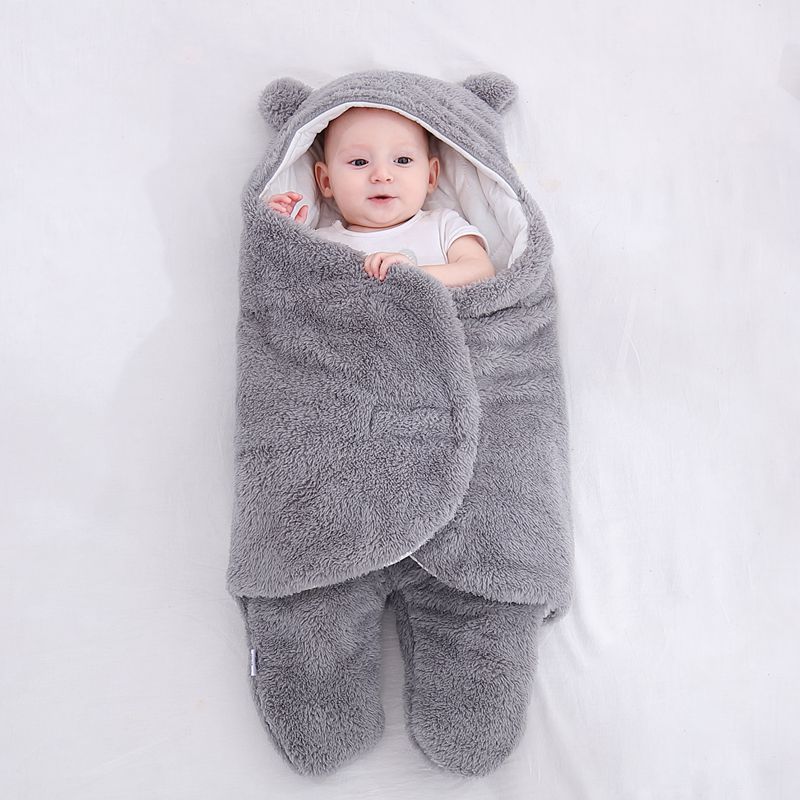 Baby wrapped in a gray fluffy swaddle with bear ears on a white background