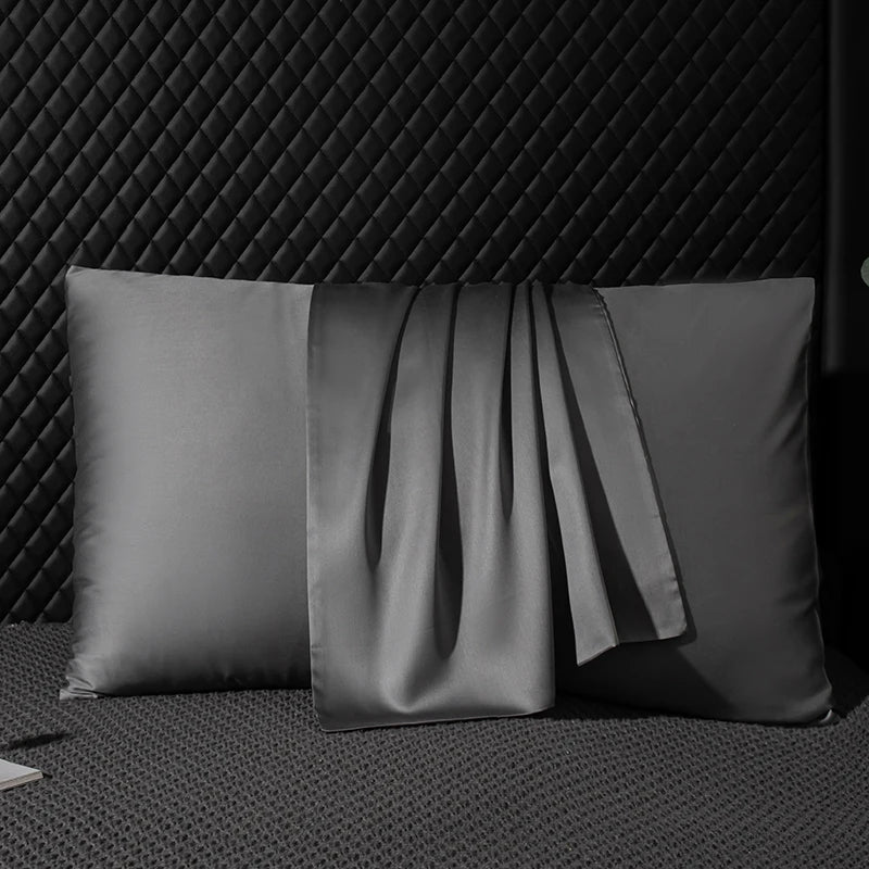 Two gray satin pillows on a textured surface with a dark geometric patterned background.