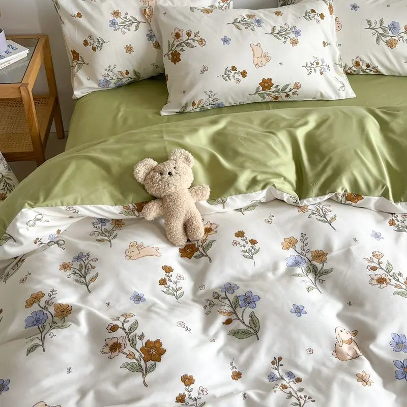 Floral and animal patterned bedding with a teddy bear on a bed.