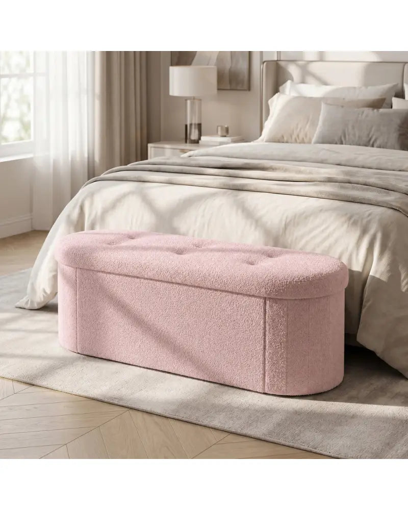A dusty pink tufted storage bench positioned at the foot of a bed in a bright, modern bedroom.