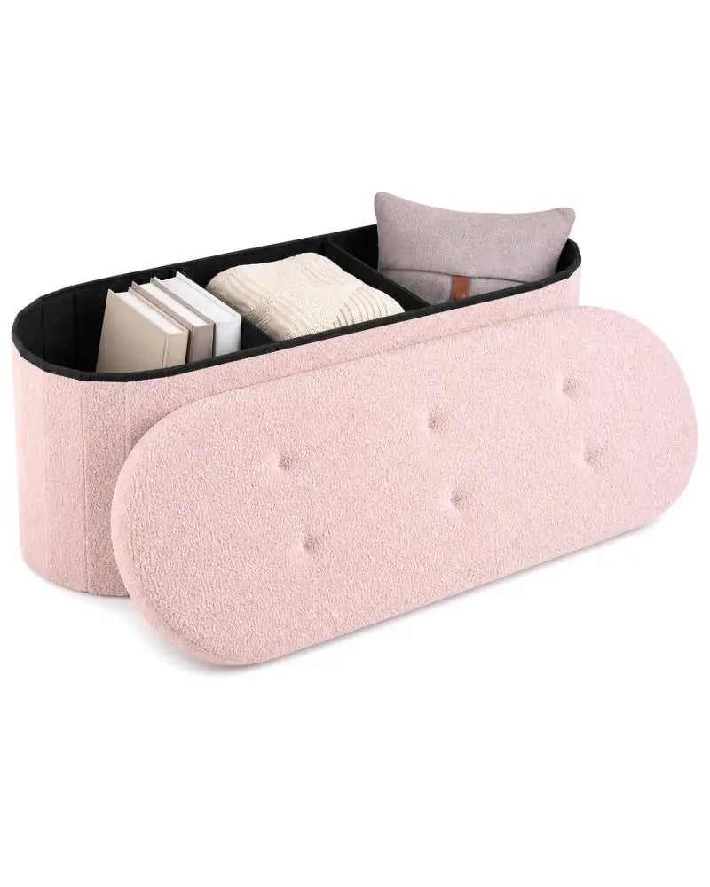 A light pink tufted storage bench with a hinged lid, shown open to reveal a black-lined compartment holding books and a folded cream textile, with a small mauve cushion inside. Photographed on a clean white background.
