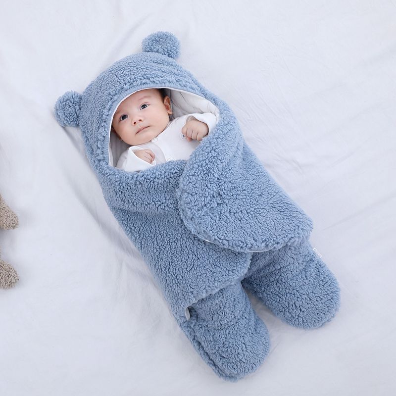 Baby wrapped in a blue fluffy blanket with bear ears on a white background
