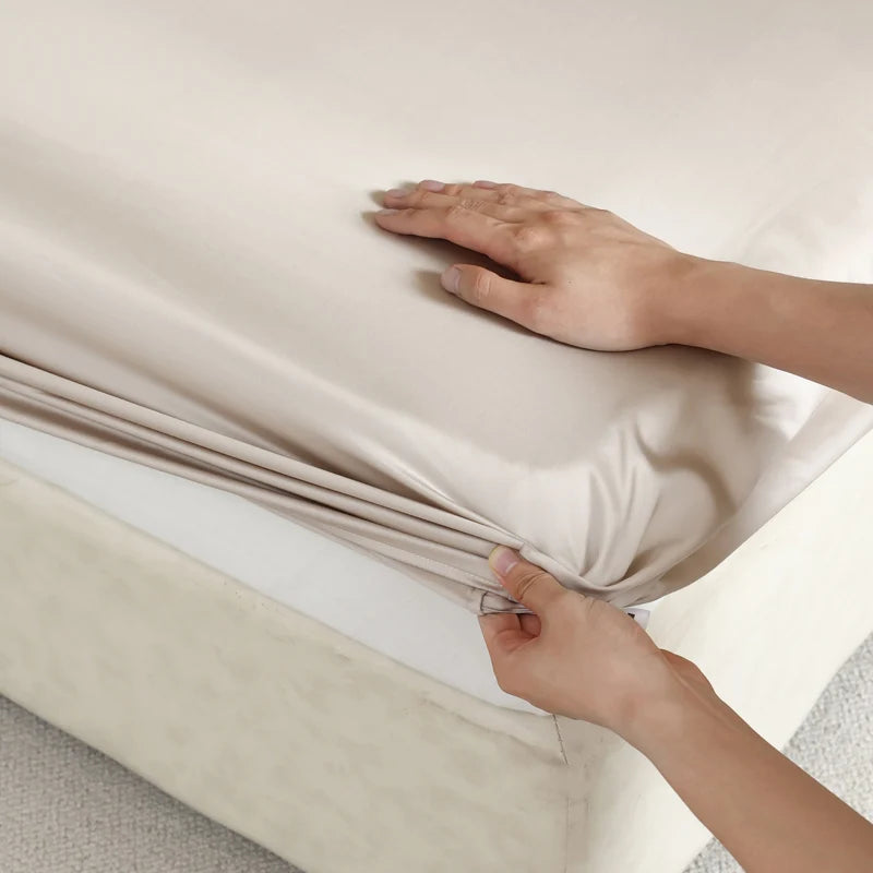 Person folding a beige satin sheet on a white background
