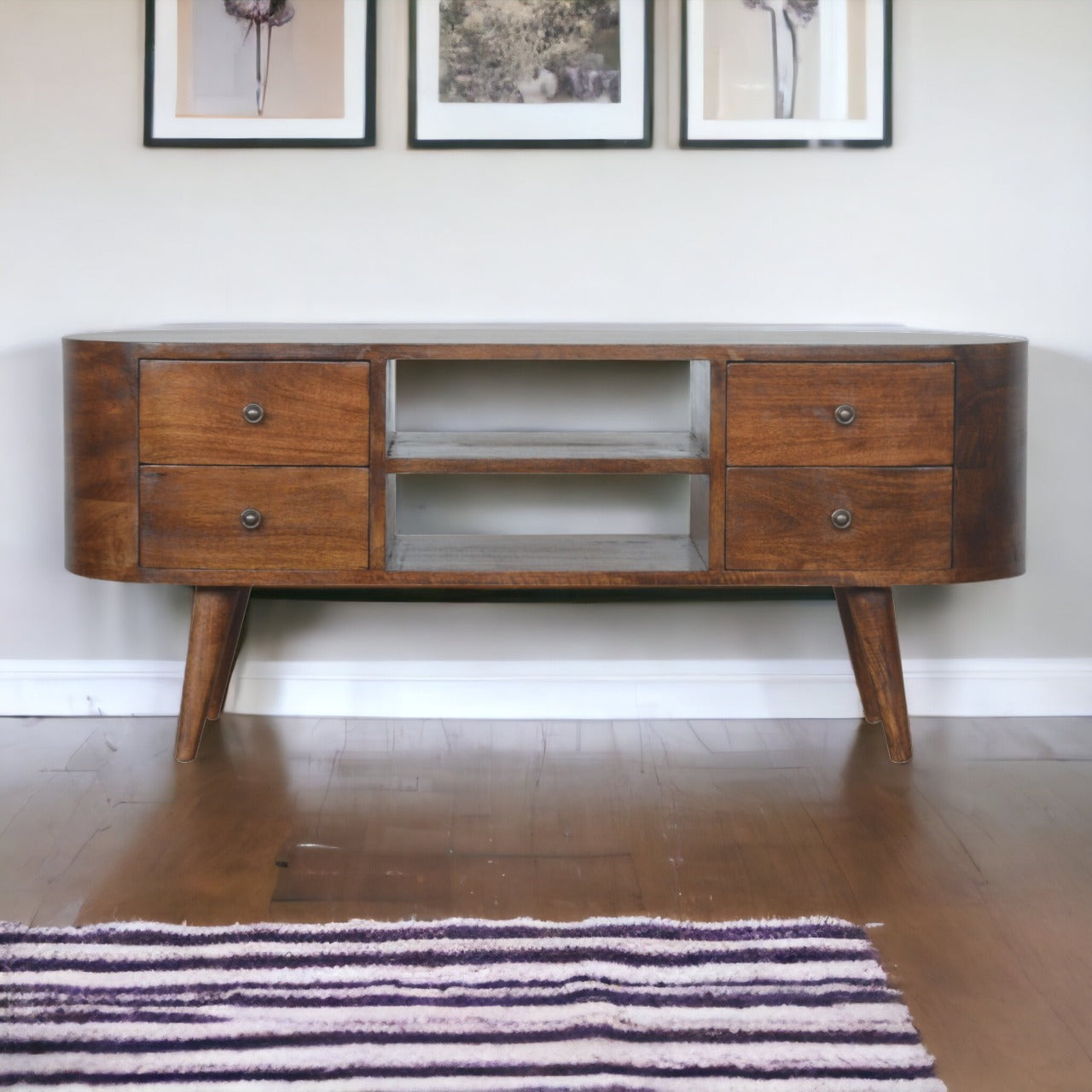 Chestnut Rounded Entertainment Unit made from solid mango wood with 4 drawers and Nordic-style legs. Full view of unit in a living space by the wall