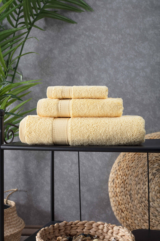 Stack of beige towels on a black surface with a gray wall and plant in the background