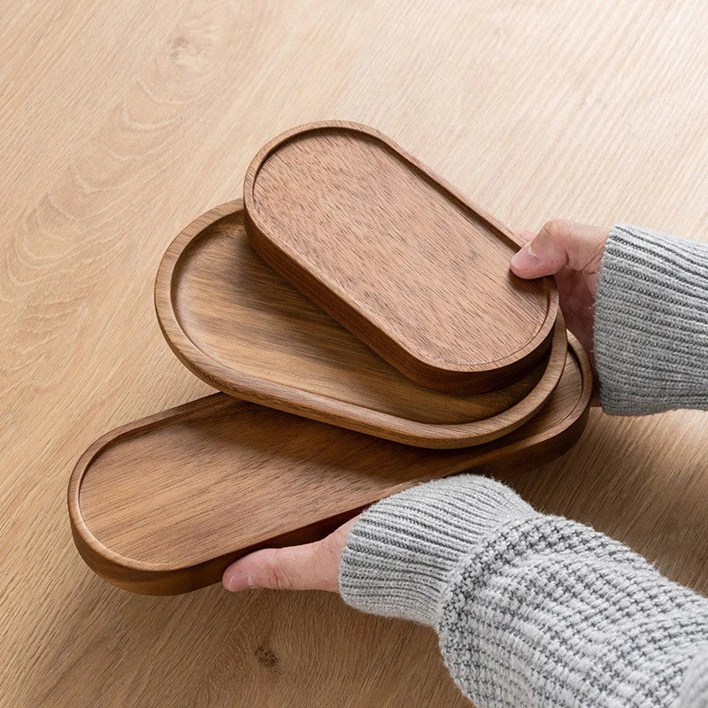 Wooden trays of different sizes on a wooden surface with hands wearing gray sleeves.
