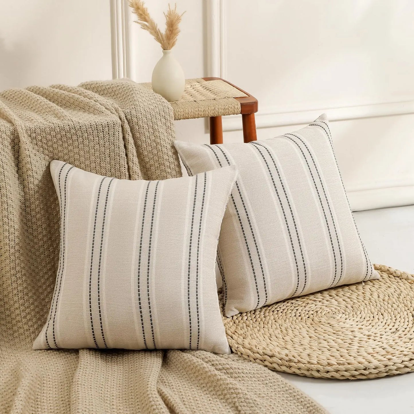 Decorative pillows with striped pattern on a sofa with a blanket and small table in the background.