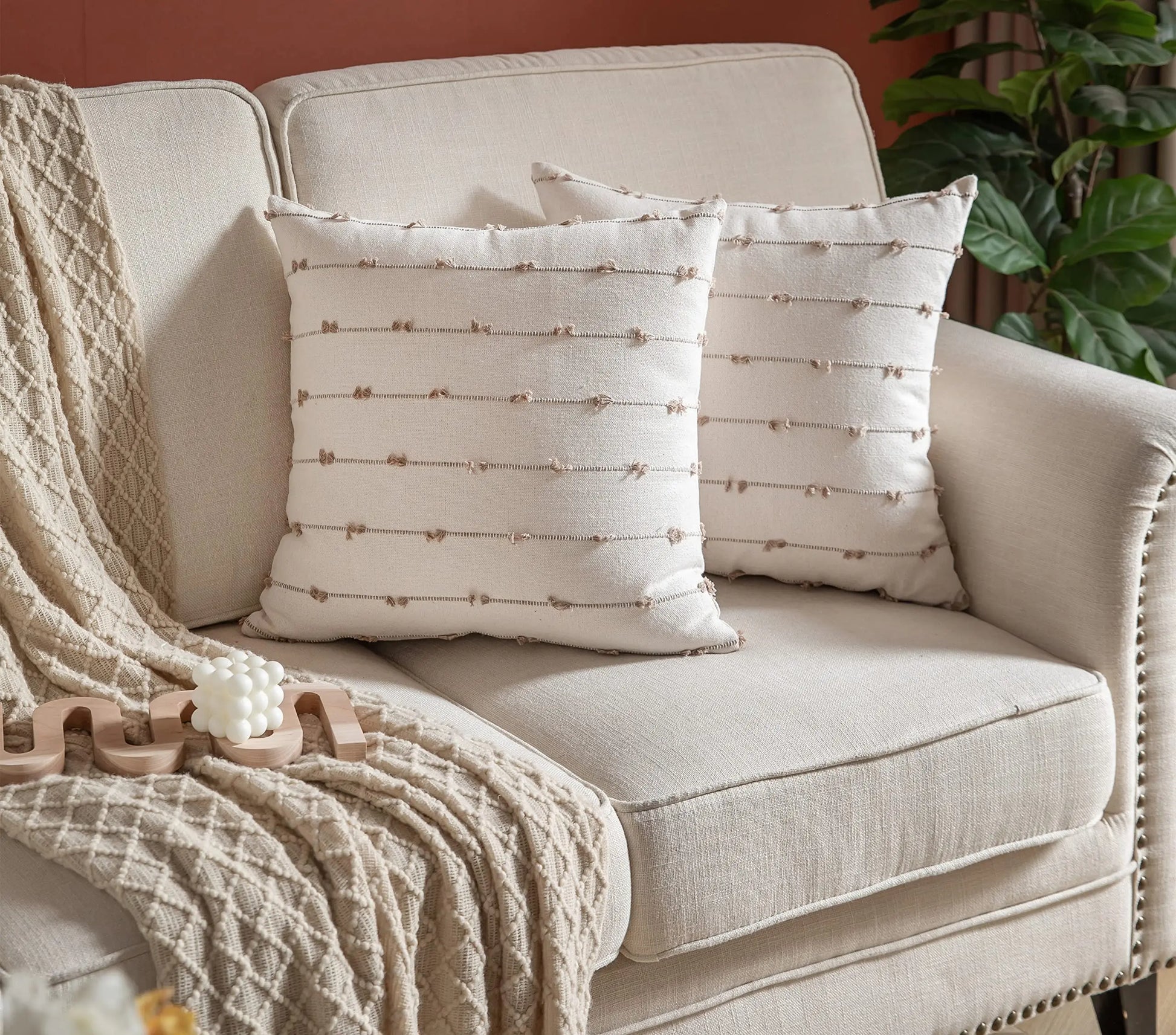 Beige armchair with patterned cushions and a blanket, against a red wall.