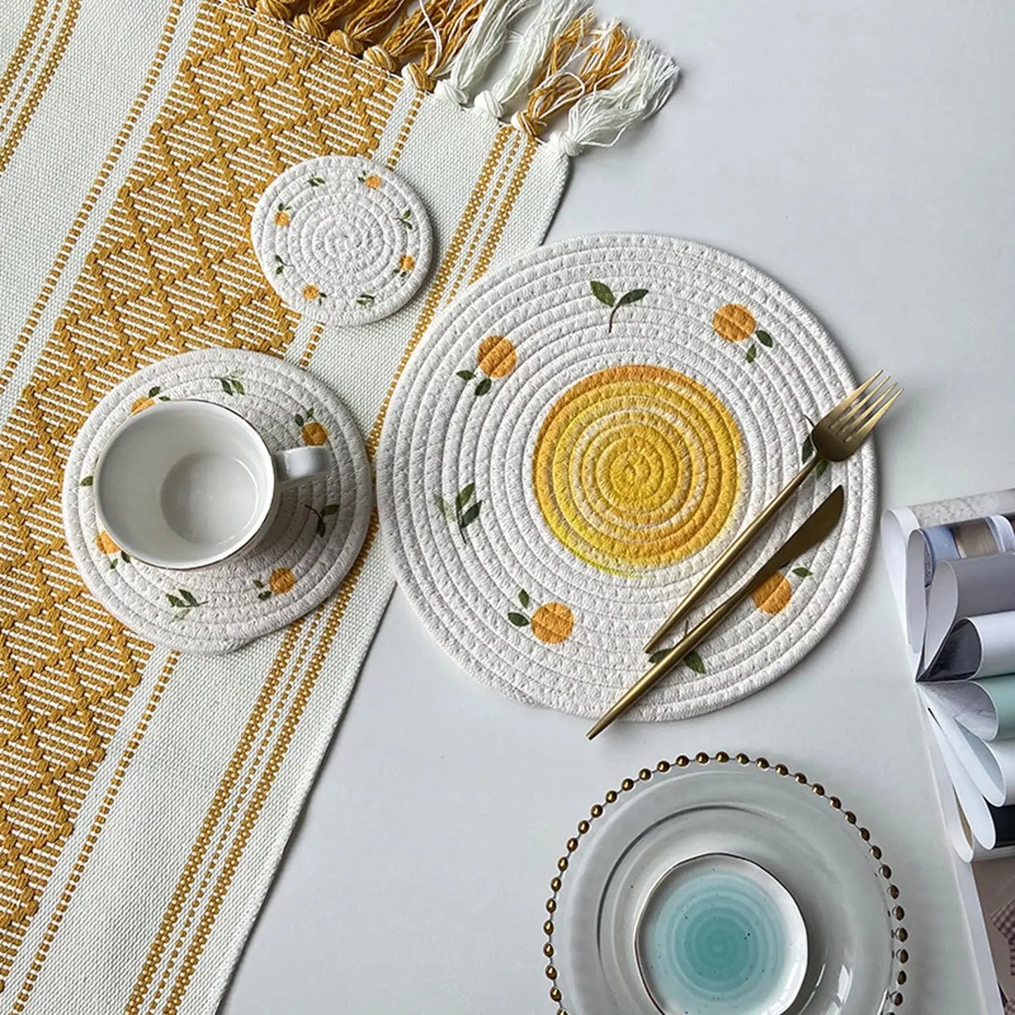 Decorative table setting with woven placemats, cutlery, and tea set on a white surface.