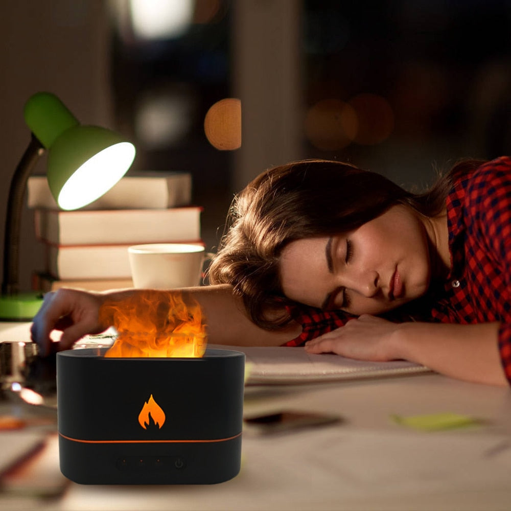 Person lying down with a small fire pit on a desk, surrounded by books and a lamp.