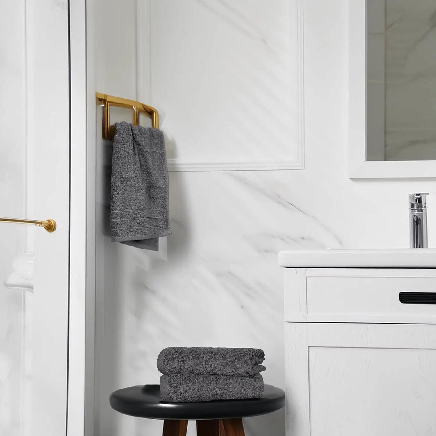 Gray towels on a black stool in a bathroom with white cabinets and marble wall.