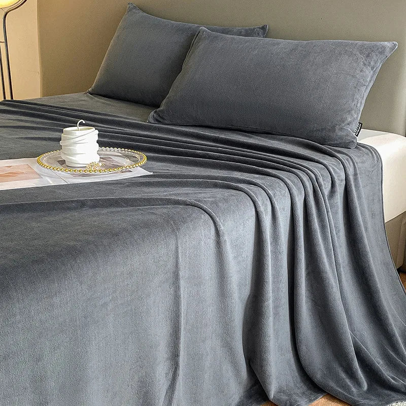 Gray bedspread and pillows on a bed with a candle and plate on a nightstand.