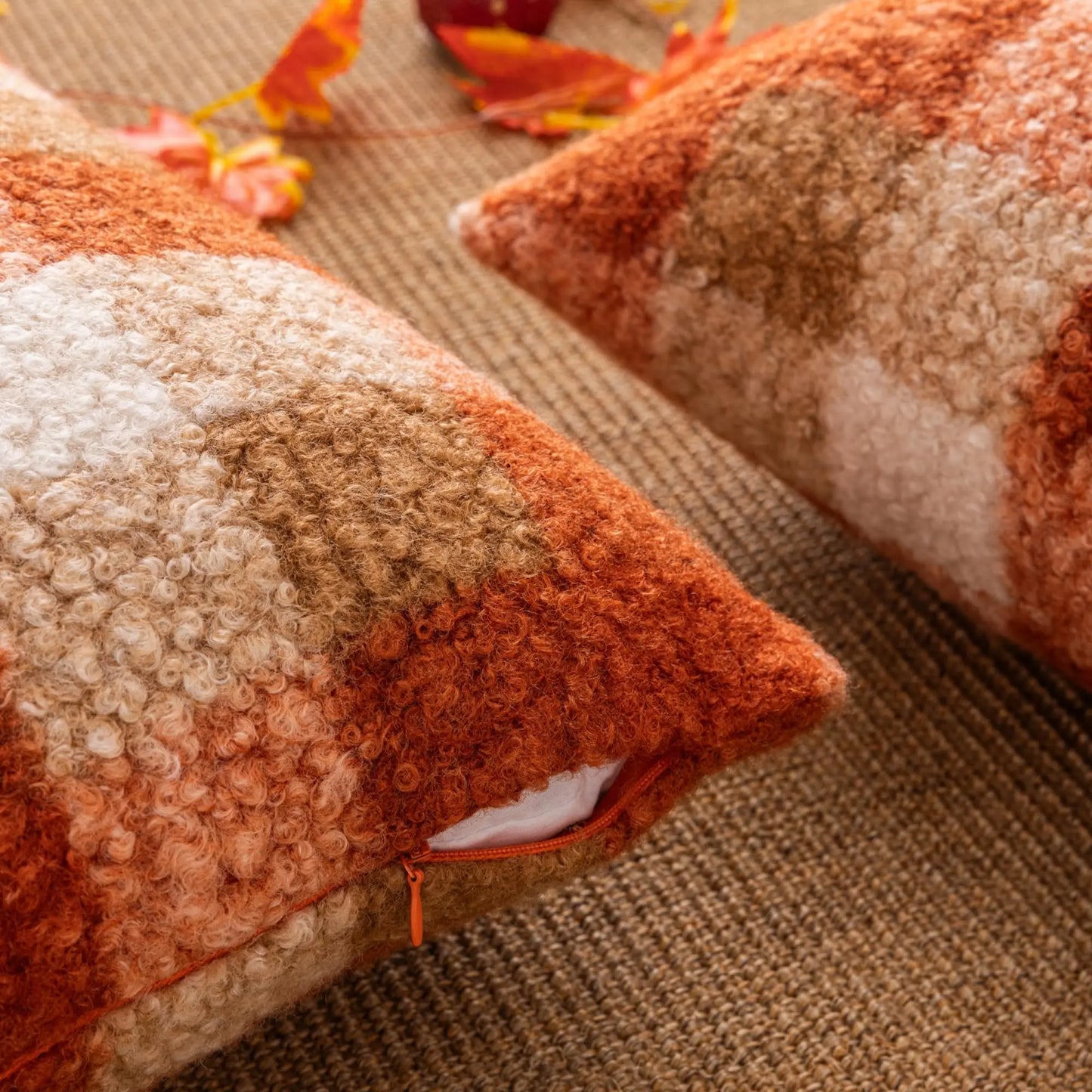 Textured orange and beige pillows on a textured surface with autumn leaves.