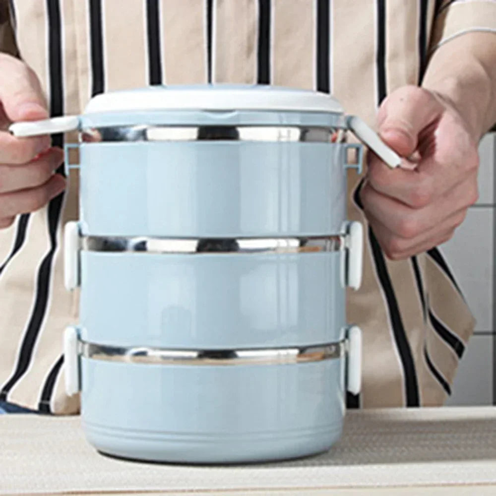 Light blue three-tiered stainless steel food container held by a person with striped sleeves.
