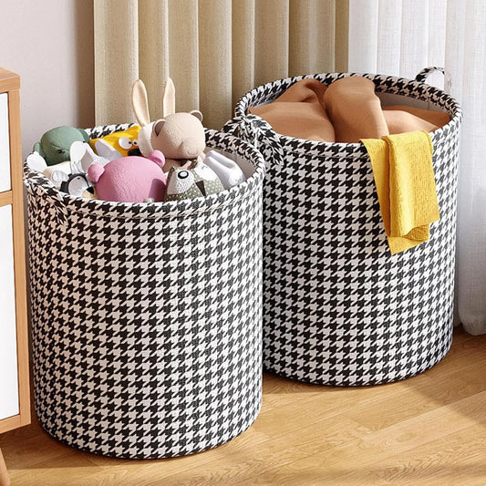 Two houndstooth-patterned storage baskets with toys and a towel on a wooden floor.