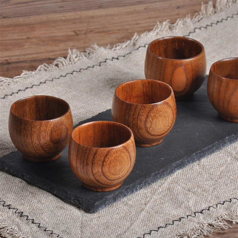Set of five wooden cups on a dark slate surface with a textured fabric background