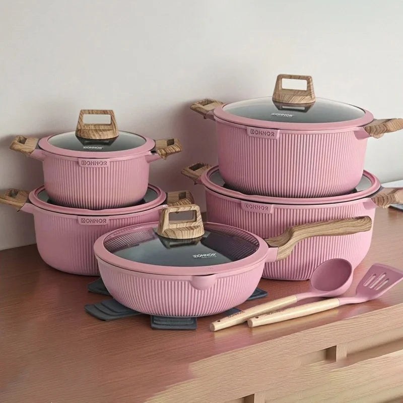 Set of pink cookware with wooden handles and utensils on a wooden surface.