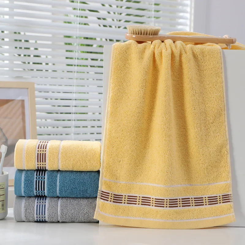 Yellow towel with decorative border on a white surface, with other towels stacked in the background.