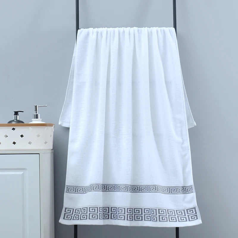 White towel with decorative border hanging on a rack in a bathroom setting.