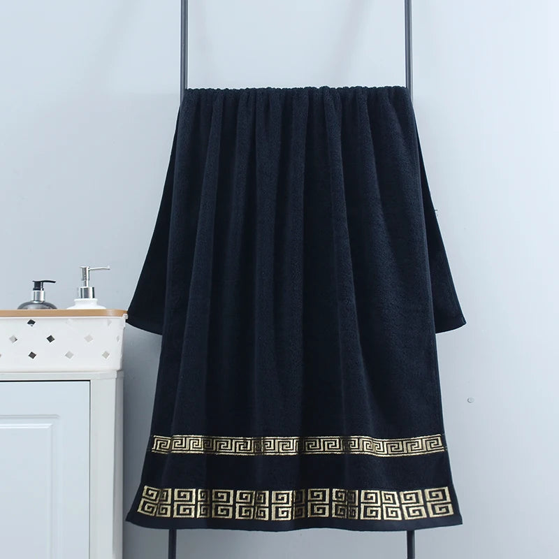 Black towel with gold patterns hanging on a rack against a white wall.