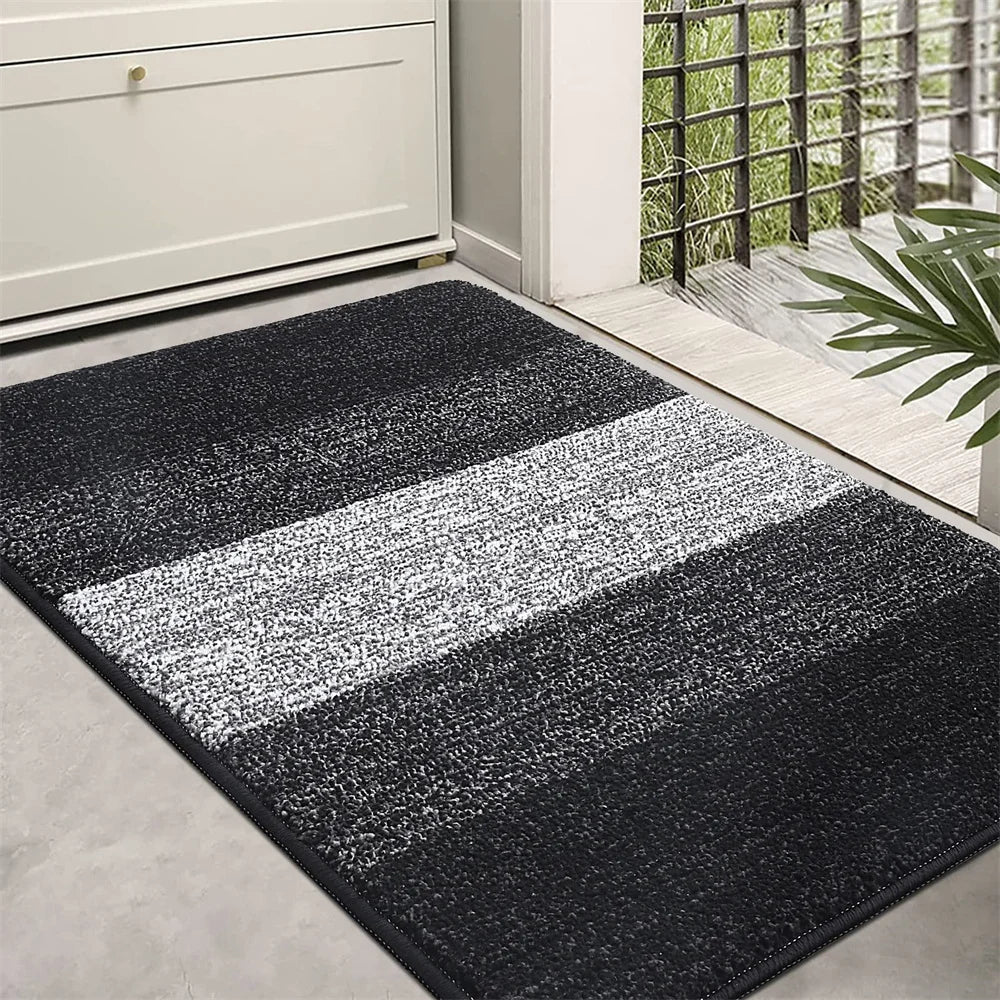 Black and gray striped doormat on a concrete floor outside a building.
