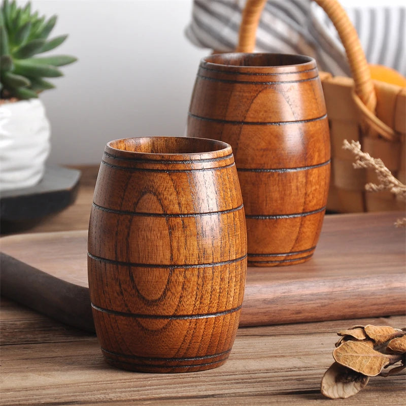 Two wooden barrel-shaped cups on a wooden surface with a plant and basket in the background.