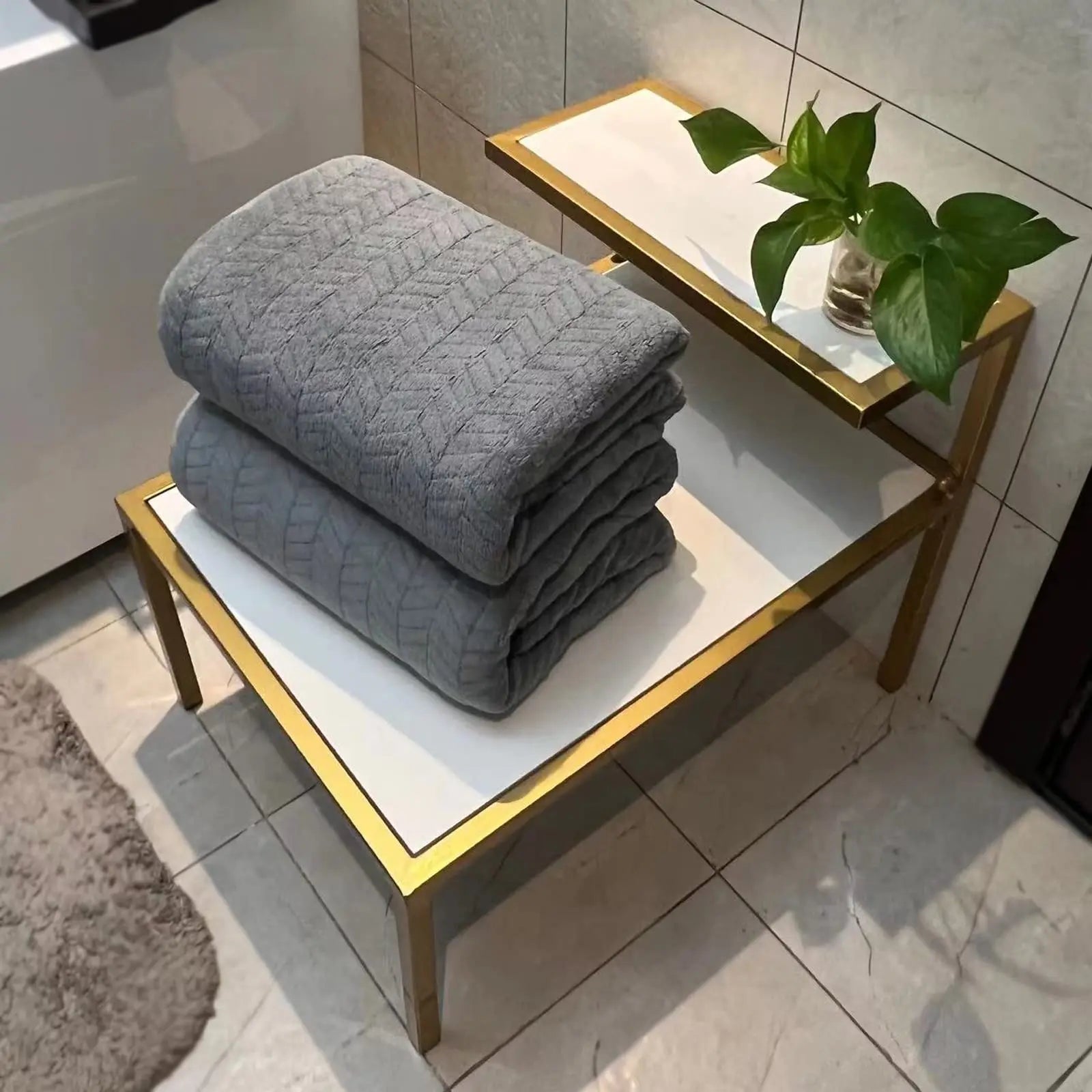 Stack of gray towels on a small table with a plant in a bathroom setting