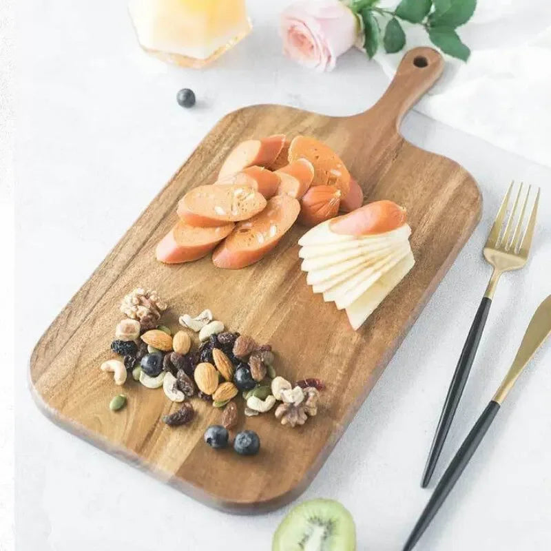Wooden cutting board with sliced fruits and nuts on a white surface with flowers and cutlery.