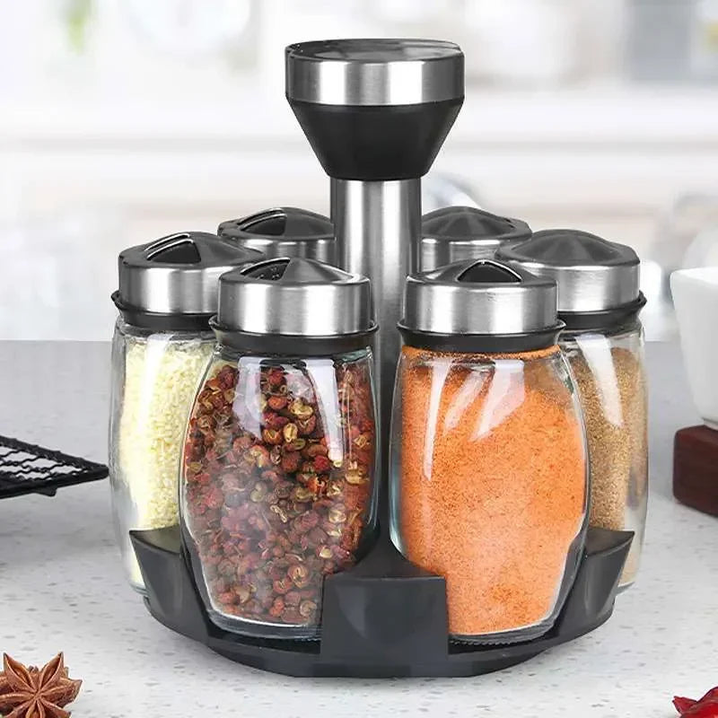 Spice rack with transparent jars containing various spices on a kitchen counter.