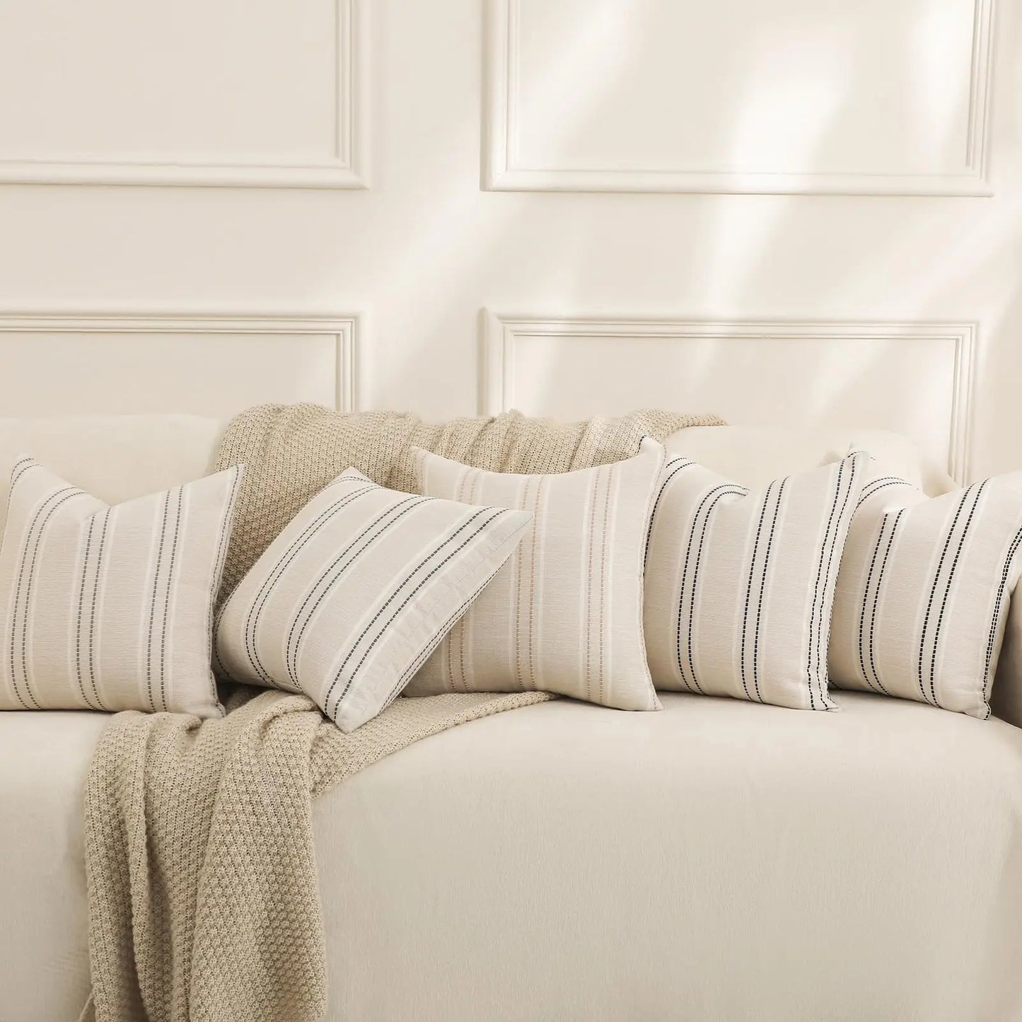Beige sofa with striped cushions and a blanket against a white paneled wall.