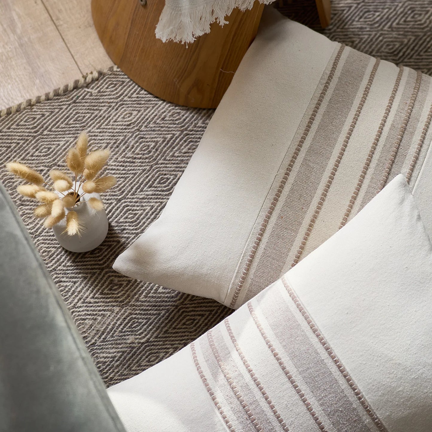 Striped cushions on a sofa with a geometric-patterned rug and a small vase with dried plants.