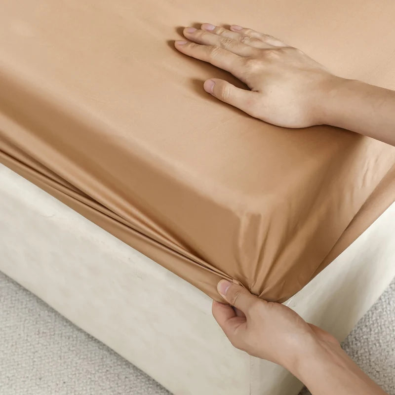 Person adjusting a brown fitted sheet on a bed