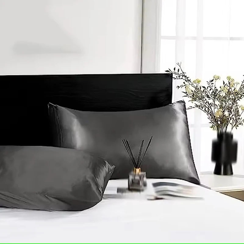 Black satin pillowcases on a bed with a minimal background
