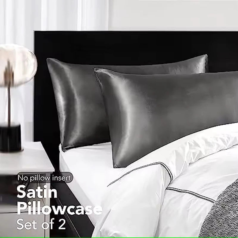 Set of two satin pillowcases on a bed with a nightstand in the background.