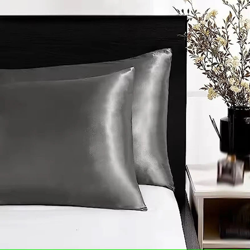 Gray satin pillowcases on a bed with a nightstand and plant in the background