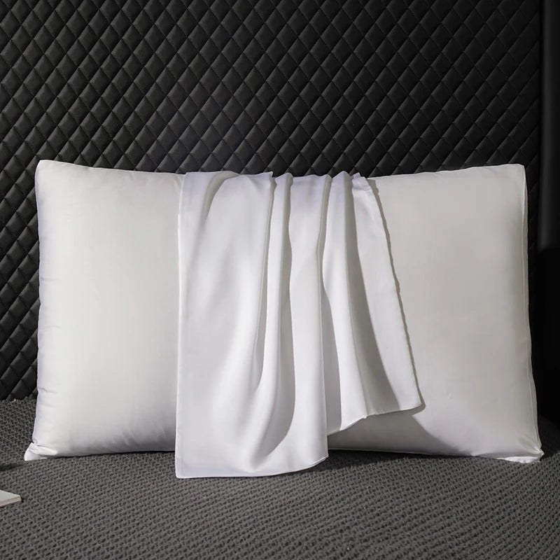 Two white pillows on a textured gray surface with a dark quilted headboard.