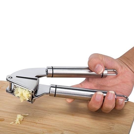 Hand using a garlic press on a wooden cutting board with a white background