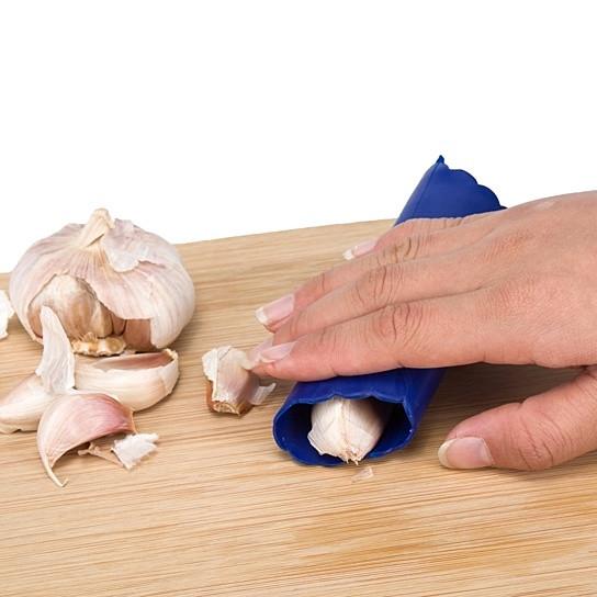 Person using a blue garlic peeler on a wooden cutting board with garlic cloves.