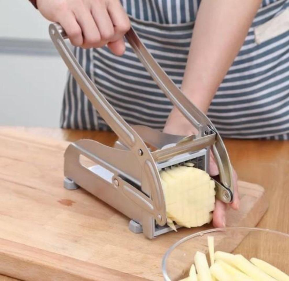 Person using a manual potato peeler on a potato with a clear bowl of peeled potatoes on a wooden surface.